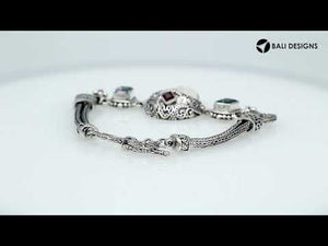 Sterling Silver bracelet featuring a carved bone face centerpiece, Garnet Quartz and Blue Topaz Quartz stones, detailed scroll panels, and a secure toggle lock for wholesale assortments.