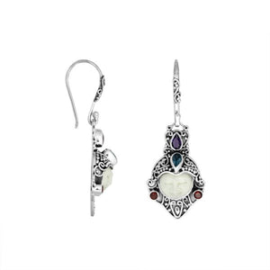 A handcrafted pair of 925 sterling silver earrings featuring carved bone faces, accented with Amethyst Quartz, Blue Topaz Quartz, and Garnet Quartz stones.