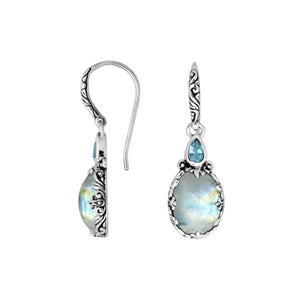 Wholesale sterling silver earrings featuring a glowing Rainbow Moonstone drop paired with a bright Blue Topaz Quartz accent and ornate carved borders for premium presentation.