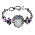 Sterling Silver bracelet featuring a carved bone face centerpiece, Garnet Quartz and Blue Topaz Quartz stones, detailed scroll panels, and a secure toggle lock for wholesale assortments.