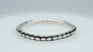 Sterling silver medium-size bangle featuring bold oval textured detailing, polished and oxidized finish, and secure hinge lock with safety latch for wholesale jewelry buyers.