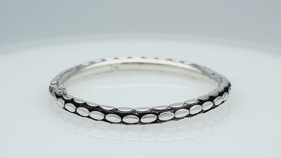 Sterling silver medium-size bangle featuring bold oval textured detailing, polished and oxidized finish, and secure hinge lock with safety latch for wholesale jewelry buyers.