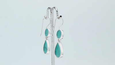 Sterling silver Turquoise Shell double drop earrings featuring circular upper settings, larger teardrop dangles, vibrant turquoise blue surfaces with dark veining, polished silver bezels, and curved fishhook earwires, shown in front and side views.