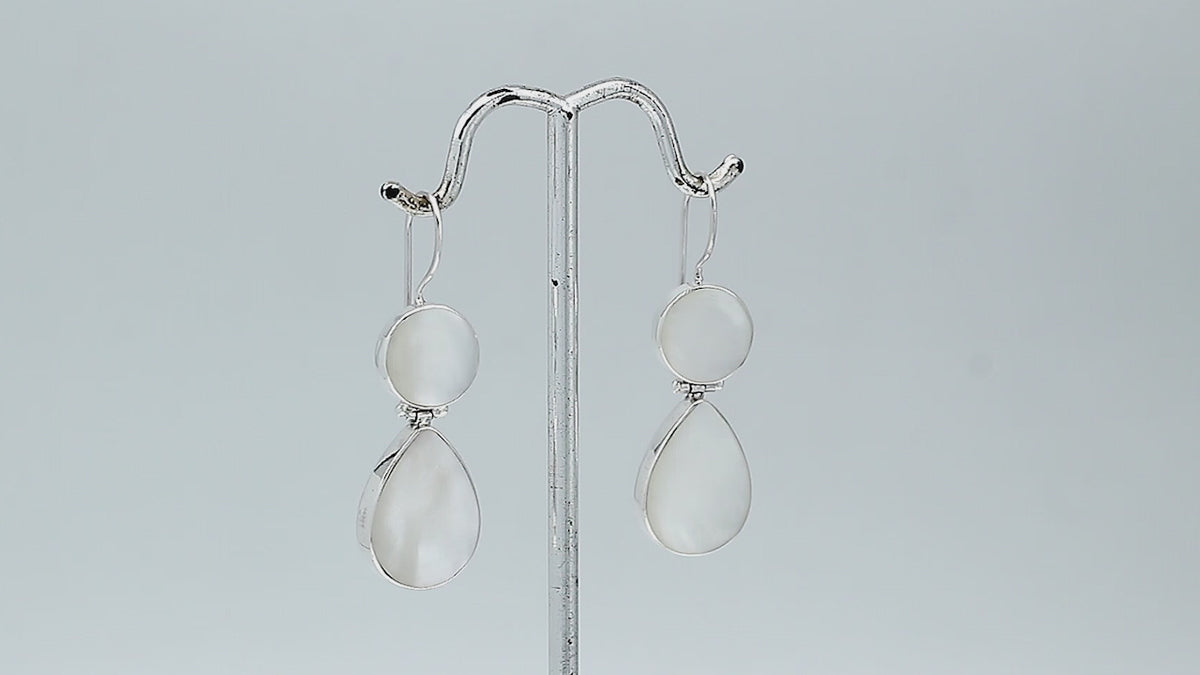 Sterling silver Mother Of Pearl dangle earrings featuring round and teardrop shell elements, polished bezel settings, articulated construction, and elegant elongated ear wires.
