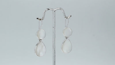 Sterling silver Mother Of Pearl dangle earrings featuring round and teardrop shell elements, polished bezel settings, articulated construction, and elegant elongated ear wires.