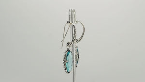 A handcrafted pair of 925 sterling silver earrings featuring faceted oval Blue Topaz Quartz stones with detailed Balinese floral motifs and secure earwire hook design.