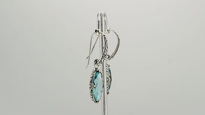 A handcrafted pair of 925 sterling silver earrings featuring faceted oval Blue Topaz Quartz stones with detailed Balinese floral motifs and secure earwire hook design.