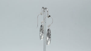 Sterling silver oval drop earrings featuring glossy Black Shell inlay, open center silhouette, sculpted scroll motifs, oxidized detailing, polished borders, and French ear wires.