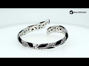 Wholesale sterling silver feather-inspired bangle featuring bold Black Shell inlays, ornate Balinese scroll engraving, and a secure hinge lock for premium artisan-inspired jewelry collections.